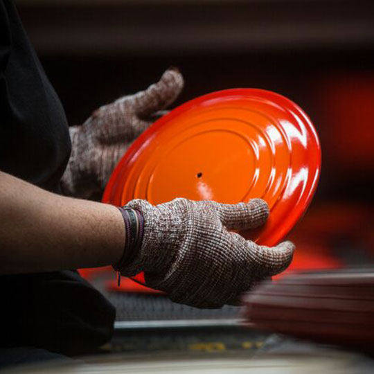 gloved hands hold a freshly manufactured dutch oven lid at the Le Creuset factory in France