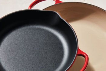 skillet with rough black enamel juxtaposed with a braiser coated in smooth sand-colored enamel