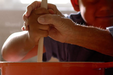 hands of older person help child's hands stir a flame orange pot