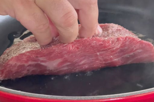 hand presses steak into skillet