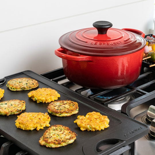 dutch oven on stove next to griddle with potato pancakes
