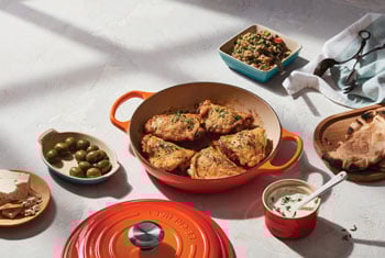 chicken in a flame orange braiser surrounded by sides and sauces