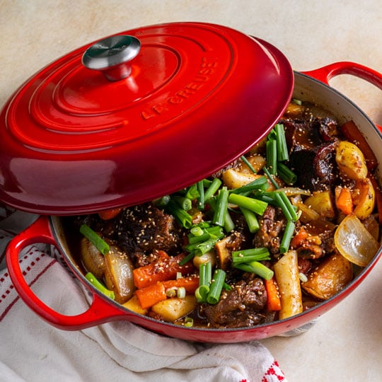 chunks of glazed beef and veggies in a cerise red braiser
