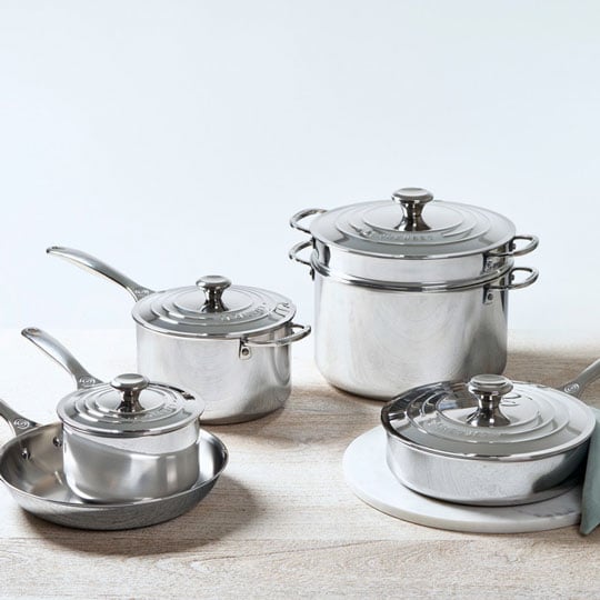 large set of stainless steel cookware arrayed on a butcher block countertop