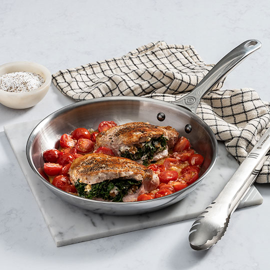 pork chops surrounded by tomatoes in a stainless steel fry pan
