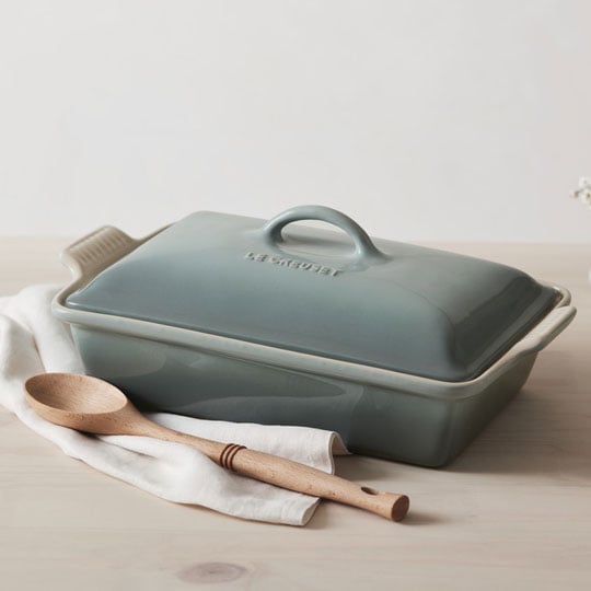 sea salt light green covered rectangular casserole next to a wooden spoon on a light wood countertop