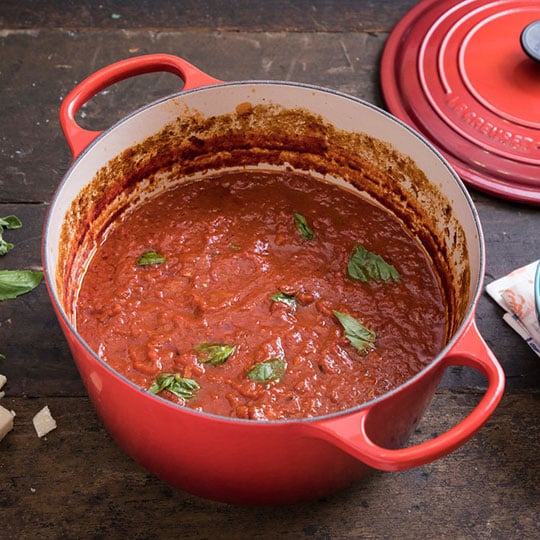 tomato sauce in a dutch oven topped with torn basil leaves