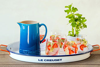 strawberry garnished glasses filled with ice alongside a blue stoneware pitcher