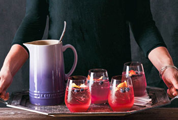 A tray of hot pink cocktails alongside a purple stoneware pitcher