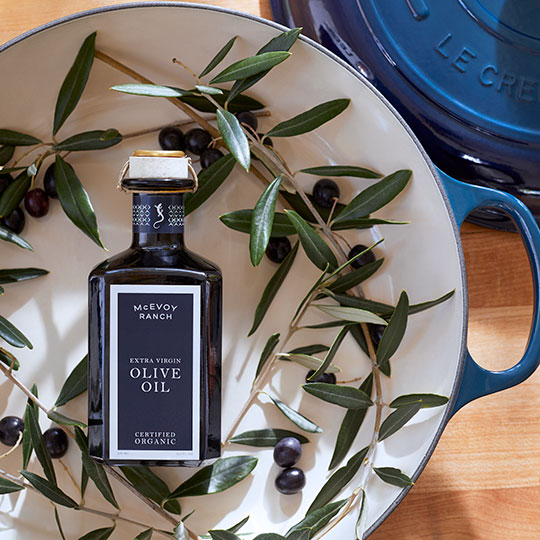 mcevoy ranch olive oil bottle in a dutch oven surrounded by olive branch twigs