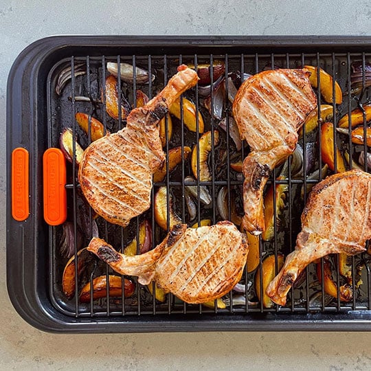 pork chops on a roasting rack above onion and peaches on a sheet pan