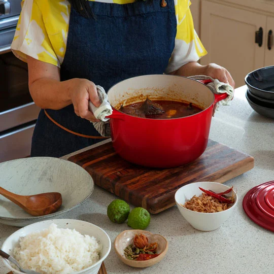 a woman places a dutch oven filled with soup on the table