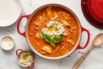 cheese and basil topped soup in a wide dutch oven