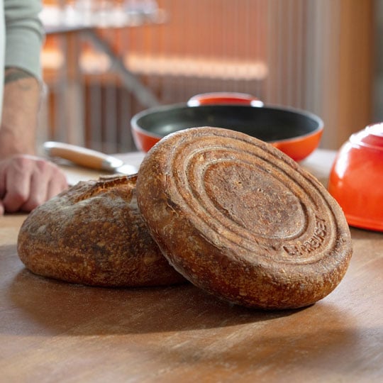 two loaves of freshly baked bread in front of a Le Creuset bread oven