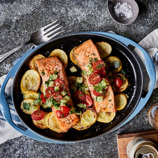salmon surrounded by veggies in a grill pan