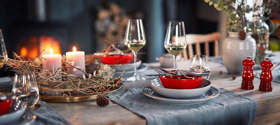 tablescape of Le Creuset dinnerware, lit candles and rustic fall accents