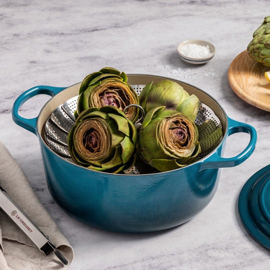 dutch oven fitted with a steamer basket holding artichokes
