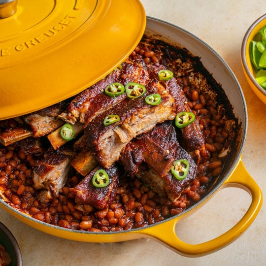 baked beans topped with sauced ribs in a yellow braiser