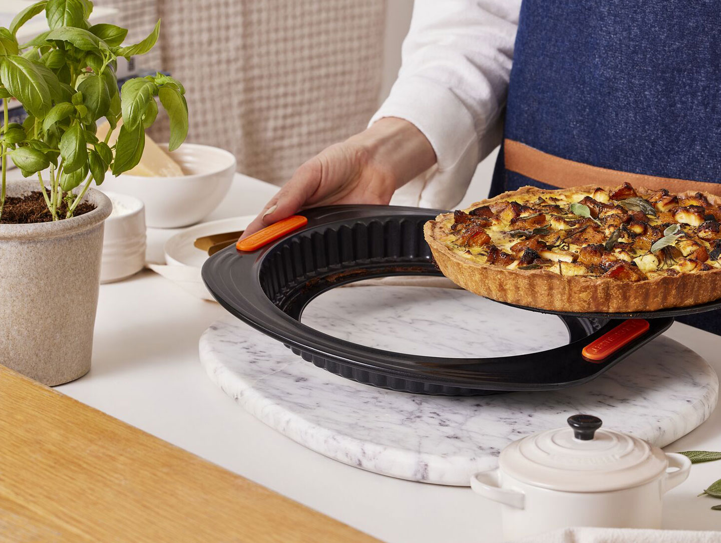 person in apron prepares quiche in a Le Creuset nonstick tart pan